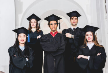 cheerful students in graduation gowns standing with crossed arms in university cheerful students in graduation gowns standing with crossed arms in university